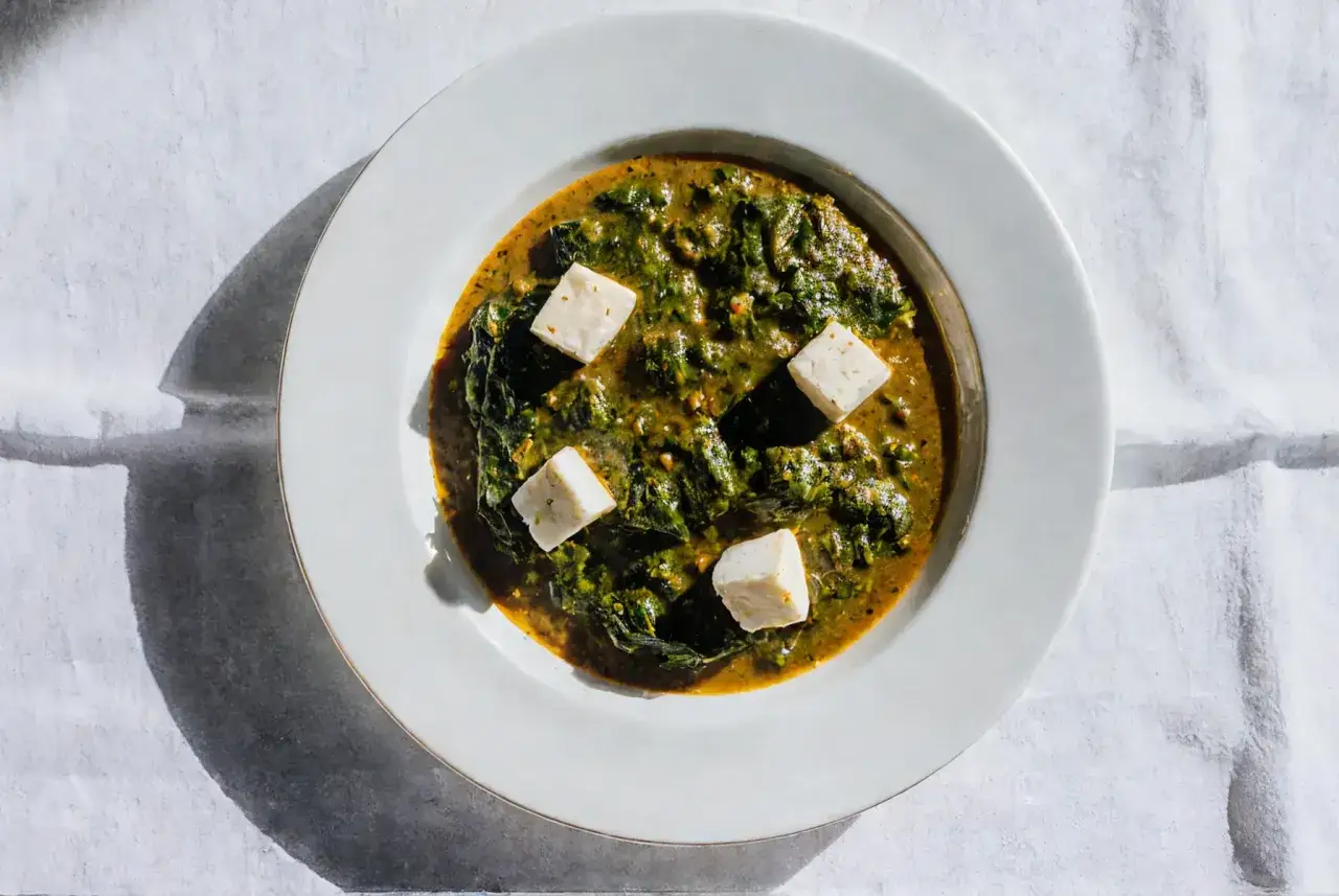 Palak paneer w białej misce, z kostkami sera paneer pływającymi w zielonym sosie ze szpinaku.