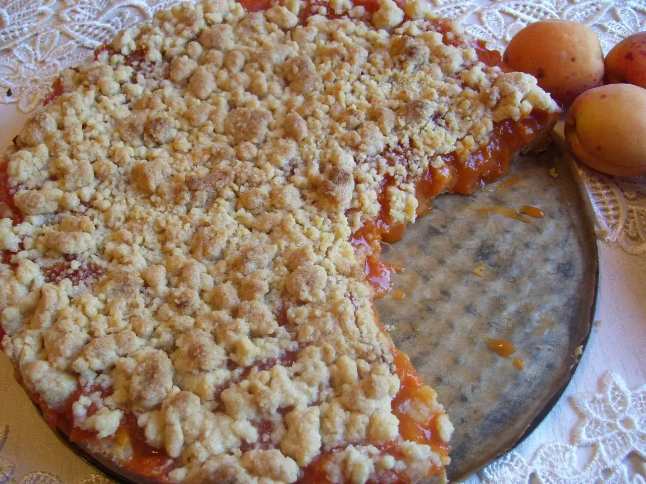 Pyszna tarta z morelami, posypana kruszonką, czeka na spr&oacute;bowanie. Obok leżą świeże morele.