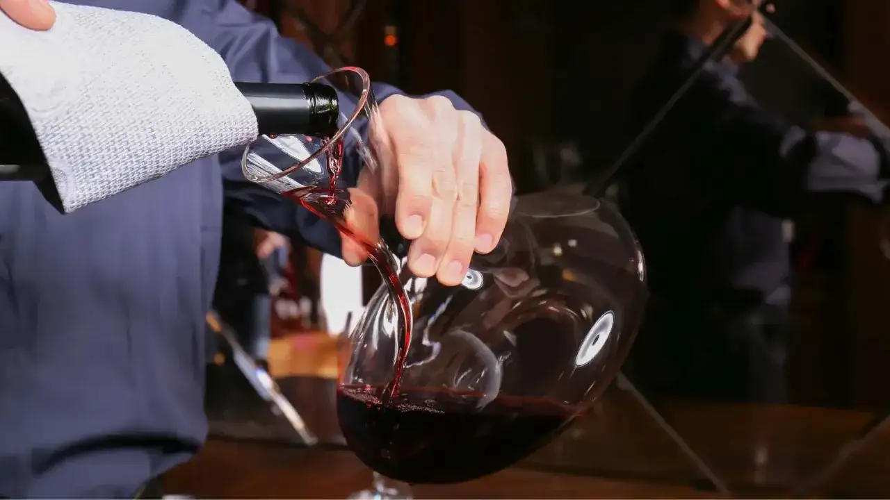 Elegancka dekantacja wina do karafki. Czerwony trunek płynie z butelki, tworząc w powietrzu rubinowy strumień.