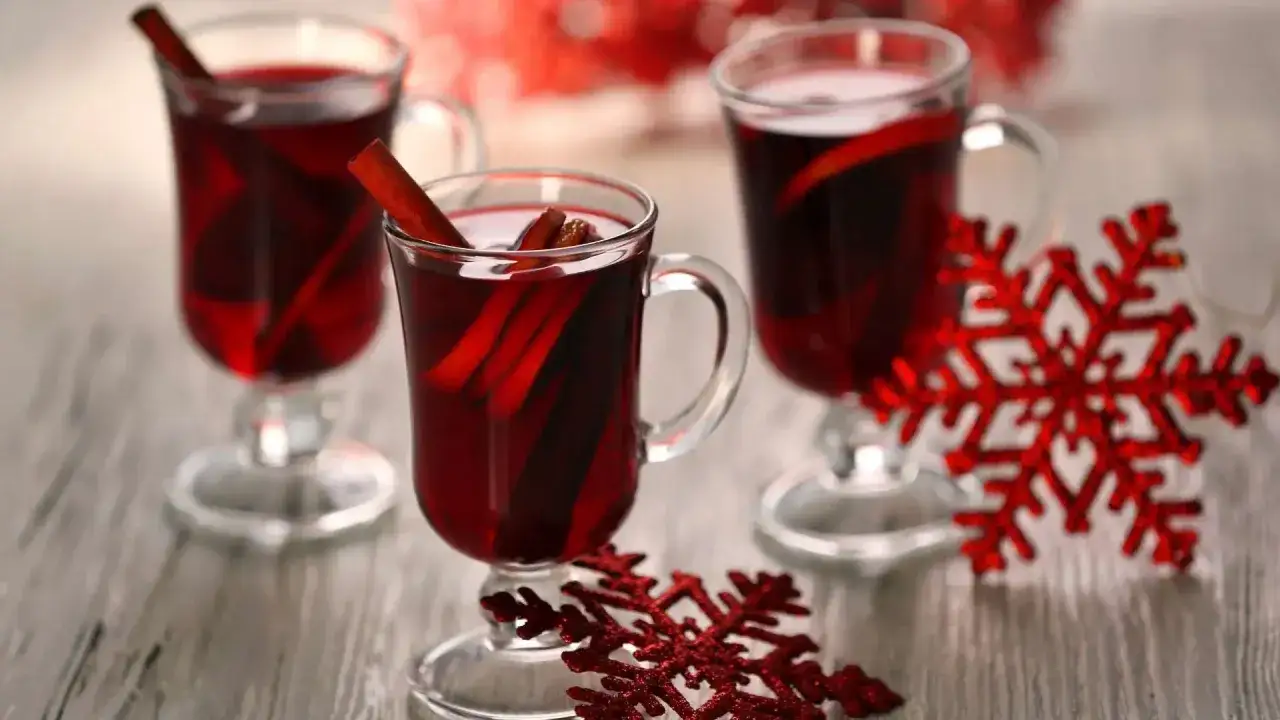 Ciepły poncz alkoholowy z laskami cynamonu w szklanych kubkach, ozdobiony czerwonymi płatkami śniegu. Idealny na zimowe wieczory.