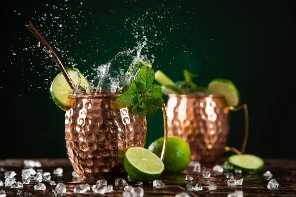 Orzeźwiający moscow mule drink z miętą i limonką, w miedzianych kubkach, z bryzgami wody i lodem.