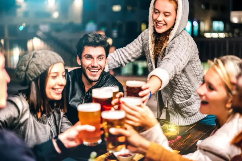 Grupa przyjaciół wznosi toasty piwem, śmiejąc się i ciesząc wieczorem. Czy piwo ma gluten? To pytanie może nurtować, ale dziś liczy się wspólna zabawa.